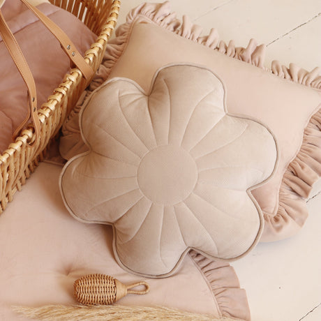 Flower-shaped pillow with ruffled edges on a soft surface, surrounded by a woven basket and decorative elements.