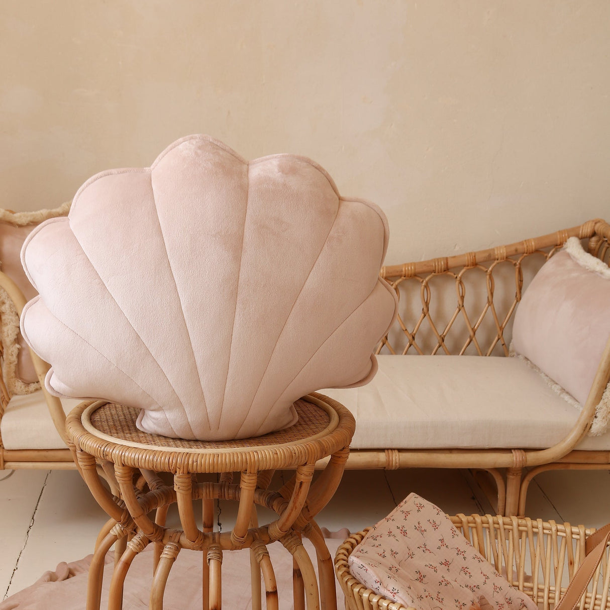 Shell-shaped cushion on a small table with a wicker chair and basket in the background.