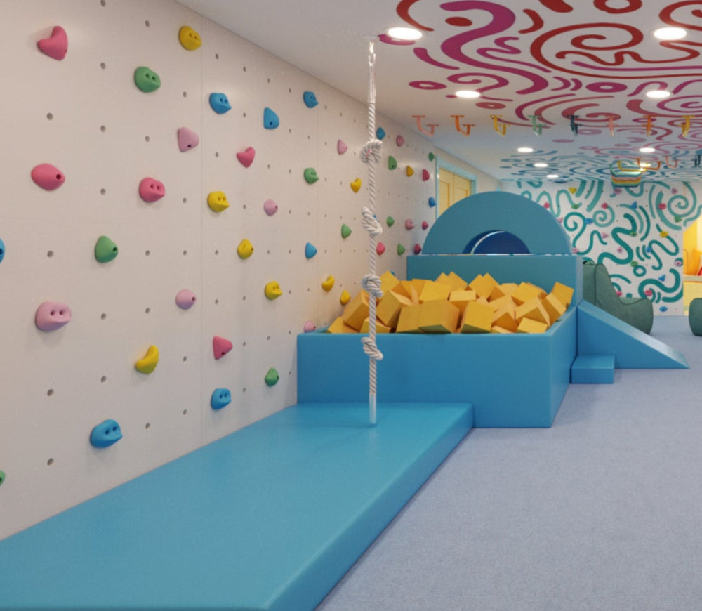 A colorful children's playroom with a climbing wall, foam pit, slide, mural walls, and a patterned ceiling.