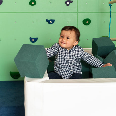 Child playing with foam cubes in a climbing area with green walls and colorful holds.