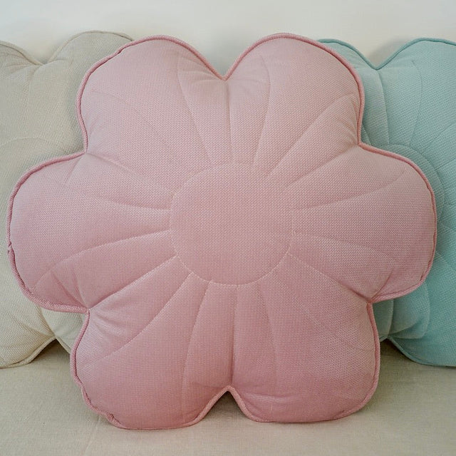 Floral-shaped pink cushion among other colorful cushions on a light background