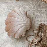 Shell-shaped pillow on a textured surface with a wicker basket and wooden sticks.