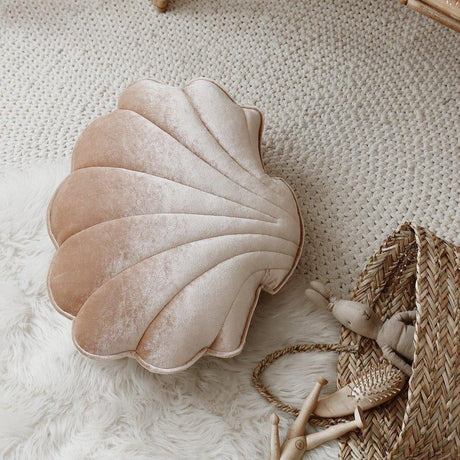 Shell-shaped pillow on a textured surface with a wicker basket and wooden sticks.