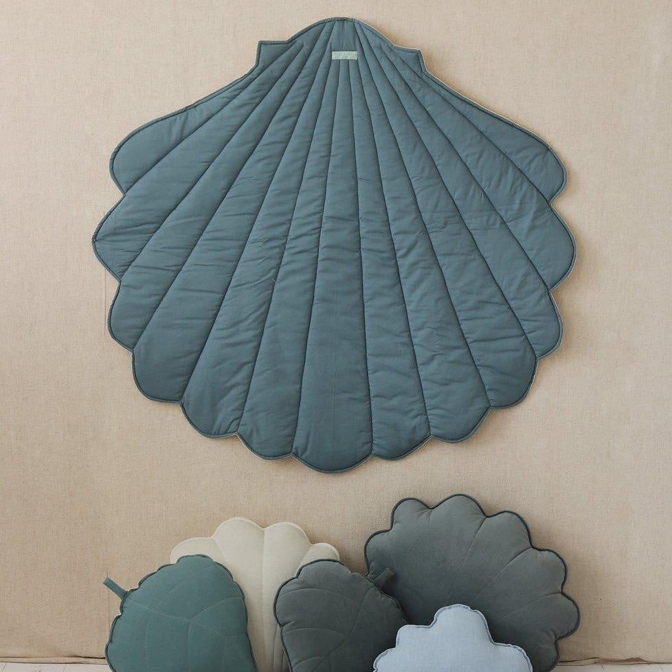 Shell-shaped teal rug on a beige wall with smaller cloud and leaf-shaped cushions below.