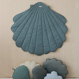 Shell-shaped teal rug on a beige wall with smaller cloud and leaf-shaped cushions below.