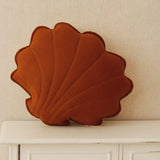 Brown shell-shaped pillow on a white surface with a beige wall background