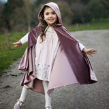 Child wearing a hooded magic cape outdoors with a castle in the background