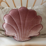 Pink shell-shaped pillow on a wicker chair with a neutral background