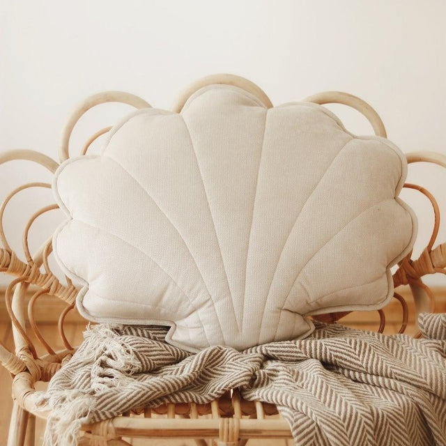 Shell-shaped cushion on a wicker chair with a blanket