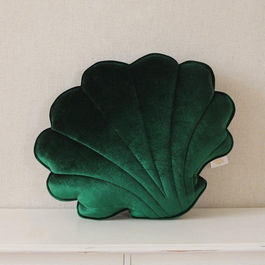Green shell-shaped pillow on a white surface with a beige wall background