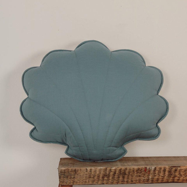 Teal shell-shaped object on a wooden shelf against a light gray wall