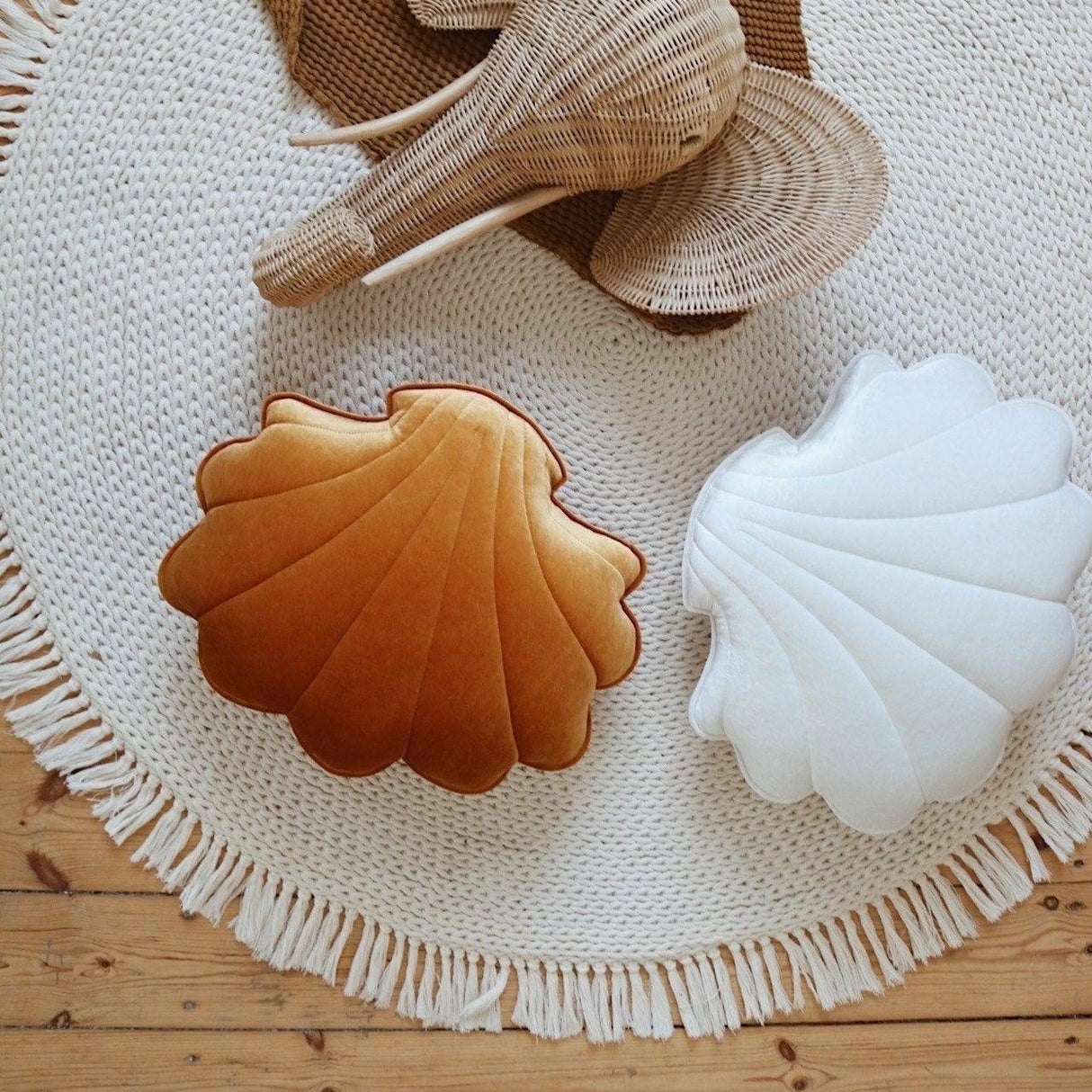 Shell-shaped cushions in brown, beige, and white on a round woven mat with a wooden floor background.