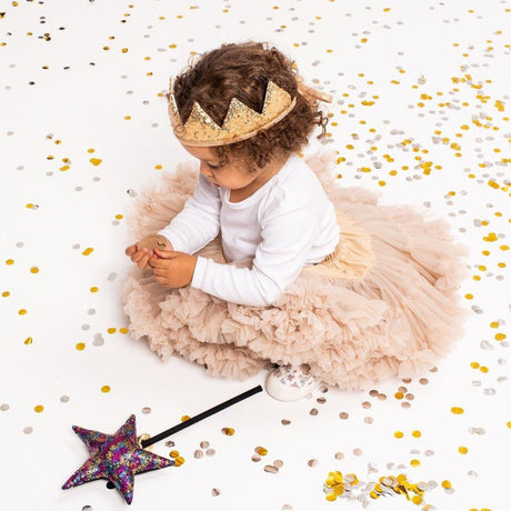 Child in a princess costume with a crown and wand on a white background with gold confetti