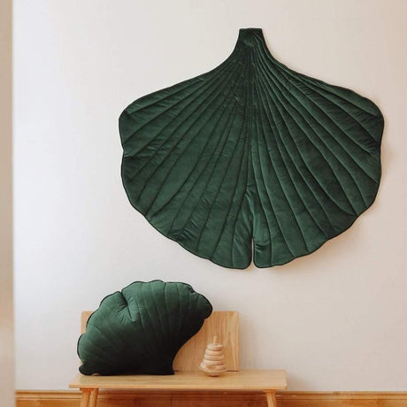 Two green leaf-shaped cushions on a wooden bench against a white wall.