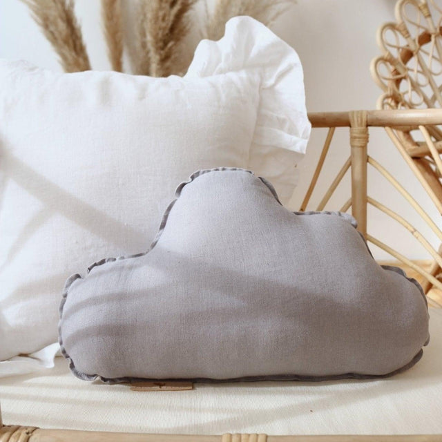 Gray cloud-shaped pillow on a wicker surface with decorative elements in the background
