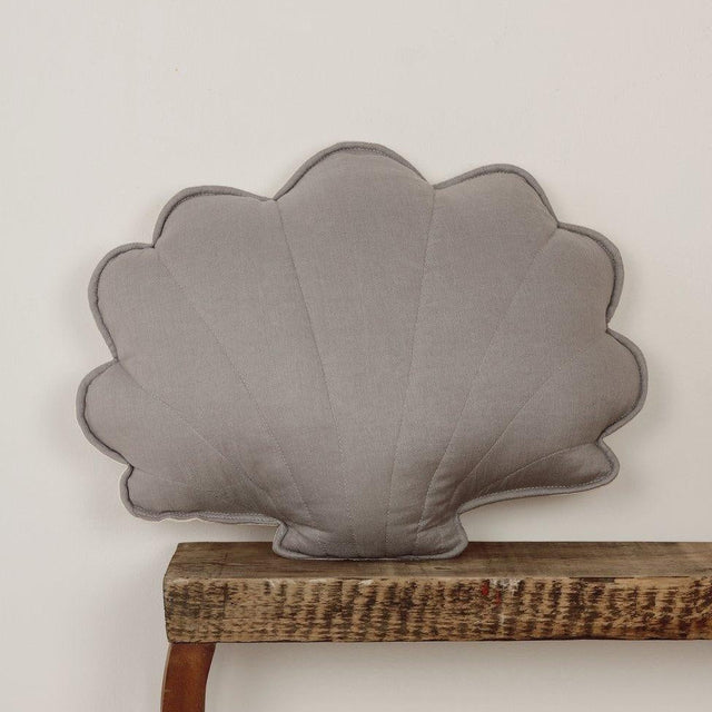 Gray shell-shaped pillow on a wooden shelf against a light gray background