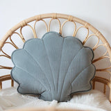 Shell-shaped blue pillow on a wicker chair with a white blanket