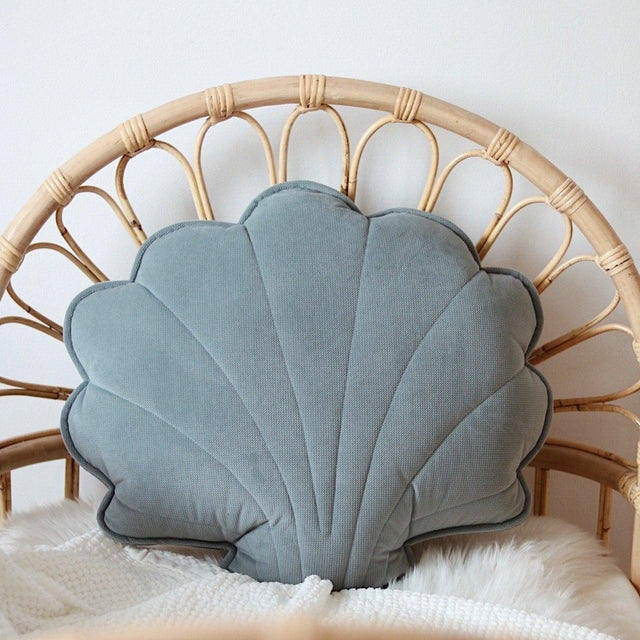 Shell-shaped blue pillow on a wicker chair with a white blanket