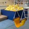 Children's swing with yellow seat in an indoor play area with soft foam blocks and climbing structures.