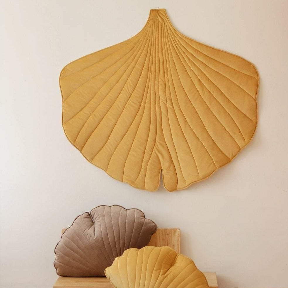 Decorative ginkgo leaf-shaped cushions on a wooden shelf against a white wall.