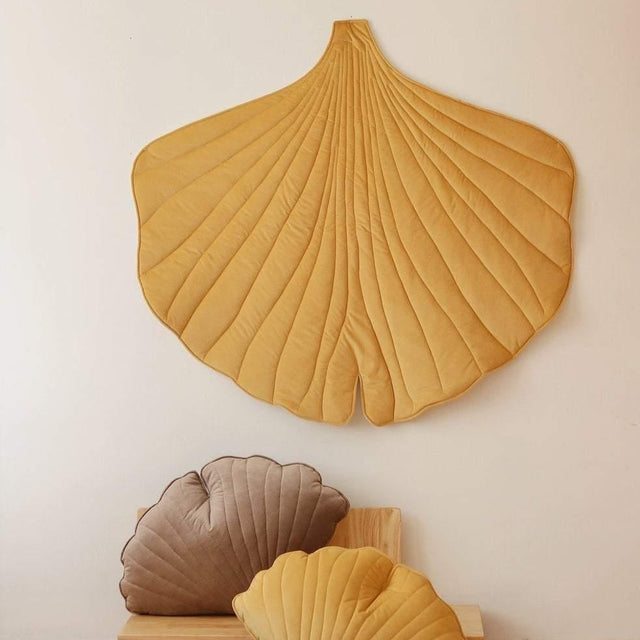 Decorative ginkgo leaf-shaped cushions on a wooden shelf against a white wall.
