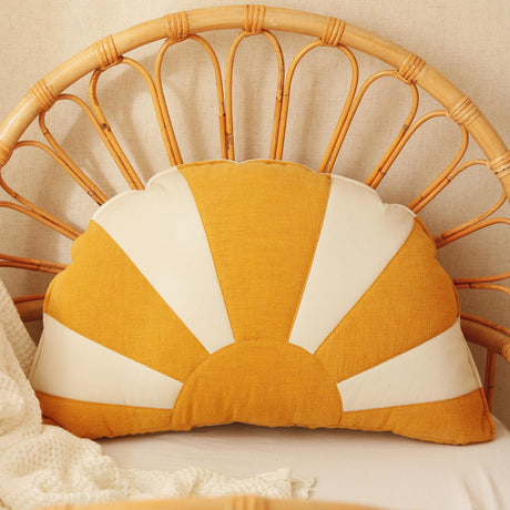 Sun-shaped pillow with yellow and white design on a wicker chair.