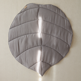 Gray leaf-shaped cushion on a beige wall