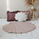 Decorative pillows and shell-shaped object on a white wooden floor with a neutral background