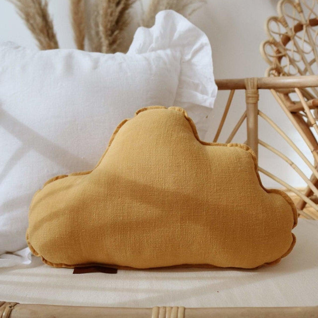 Yellow cloud-shaped pillow on a wicker surface with white pillows and decorative elements in the background.