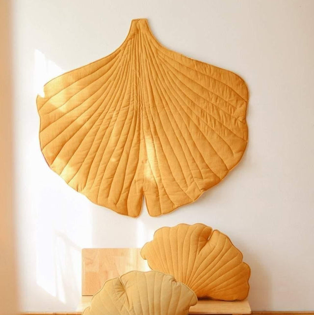 Ginkgo leaf-shaped cushions and a blanket on a wooden floor against a white wall