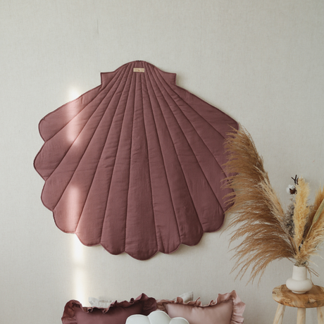 Decorative shell-shaped headboard, pillows, and rug on a white wall background