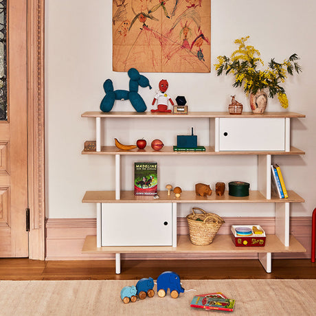 Children's playroom with a wooden shelf displaying toys and books, and a painting on the wall.