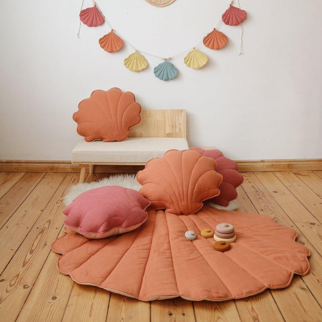 Shell-shaped cushions and a rug on a wooden floor with decorative wall hanging.
