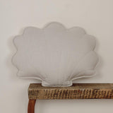 Shell-shaped cushion on a wooden shelf against a plain wall