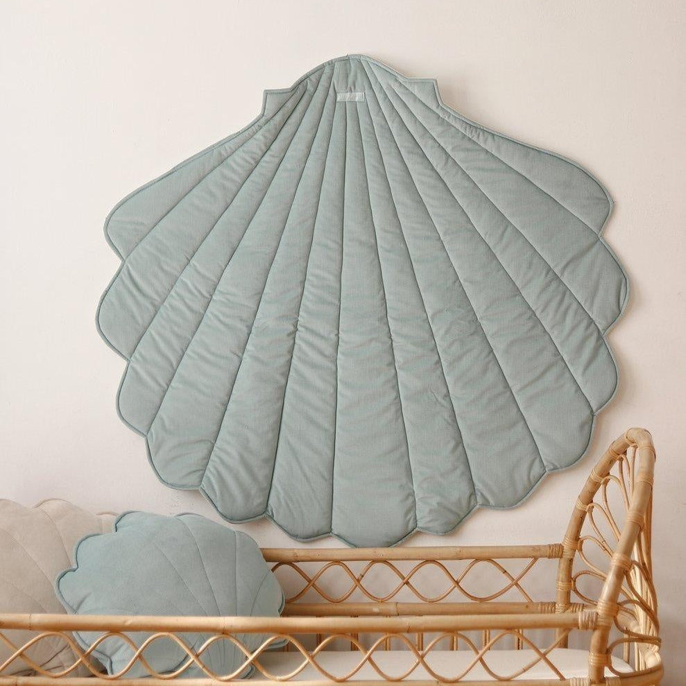 Large green shell-shaped cushion on a beige wall above a wicker chair.
