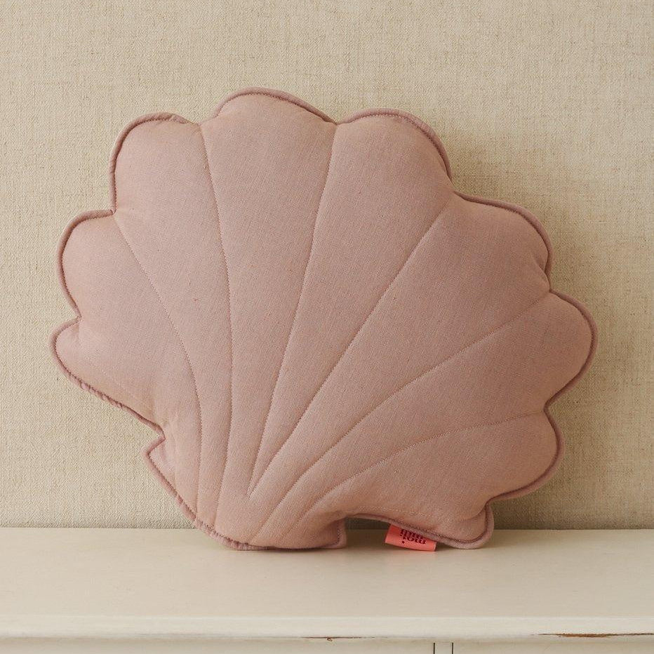 Pink shell-shaped pillow on a beige surface with a neutral background