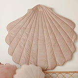 Decorative shell-shaped pillow on a white wall with a wicker chair in the foreground.