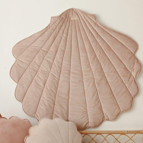 Decorative shell-shaped pillow on a white wall with a wicker chair in the foreground.