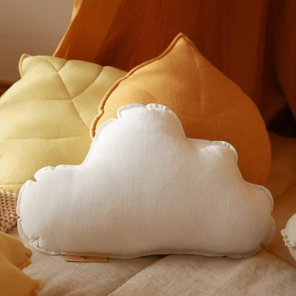 White cloud-shaped pillow on a bed with yellow and orange pillows in the background