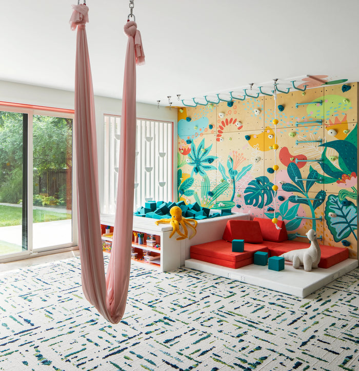 Modern playroom featuring a sensory swing next to an indoor climbing wall.