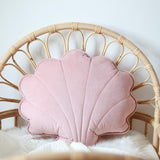 Pink shell-shaped pillow on a wicker chair with a white blanket