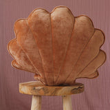 Shell-shaped cushion on a wooden stool against a pink background