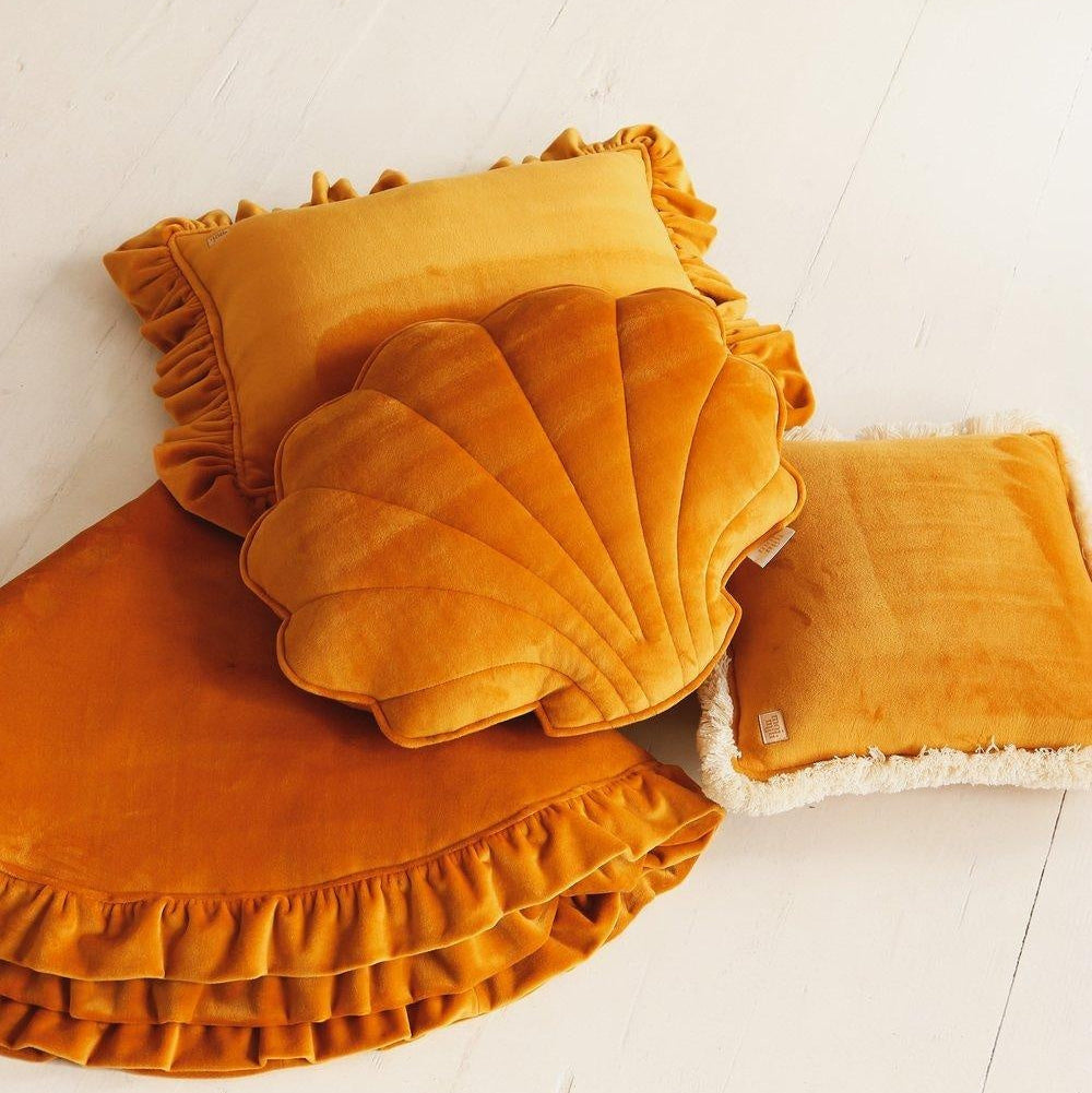 Mustard yellow shell-shaped cushion on a white floor